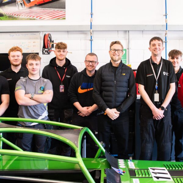A group of young men standing next to a green race car chassis in a garage.