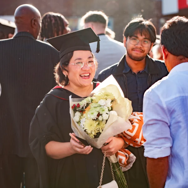 A smiling woman in graduation gown and cap holding a bouquet of flowers.