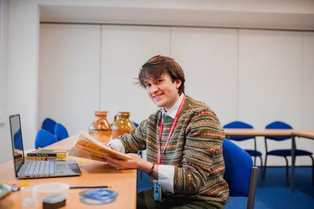 Woman sitting at a table with a laptop and books, wearing a lanyard.