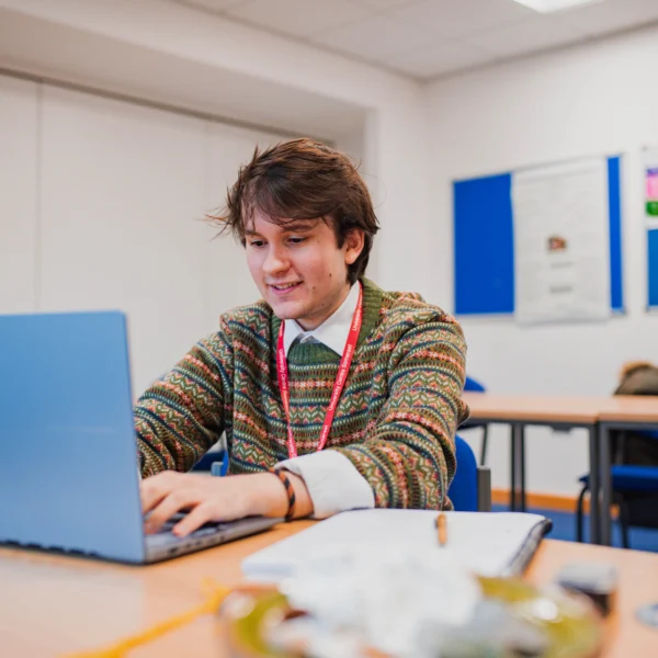 A young person focused on a laptop in a classroom.
