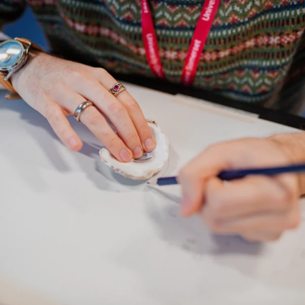 a person's hands holding a small object and a pen