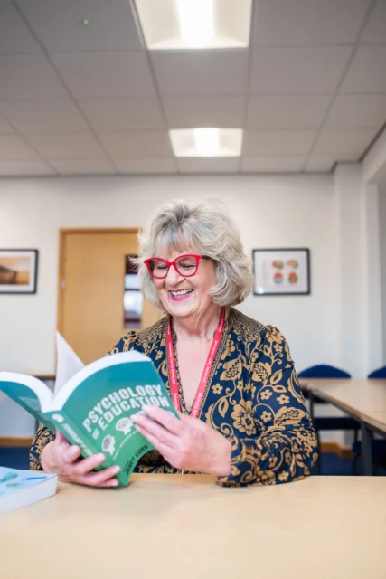 A woman reading a book titled 'The Art of Research'. She appears to be in a classroom or library setting.