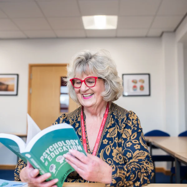 A woman reading a book titled 'The Art of Research'. She appears to be in a classroom or library setting.