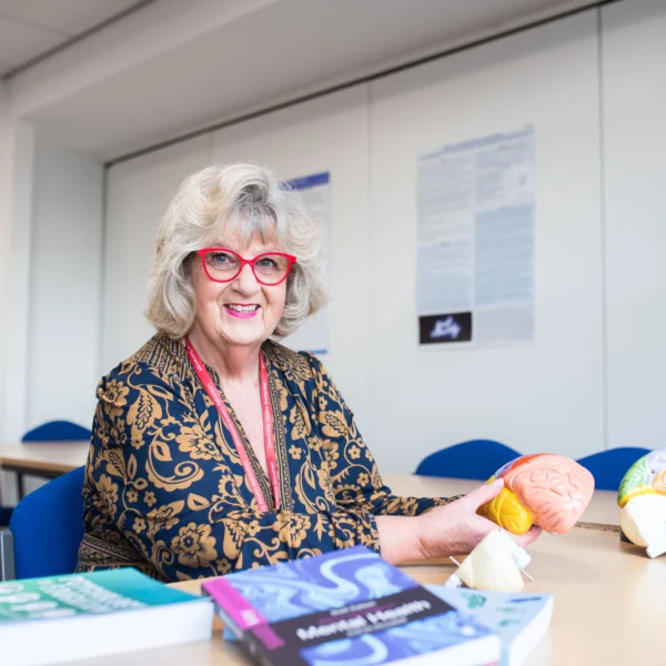 An older woman sitting at a desk with books and a model of the brain.
