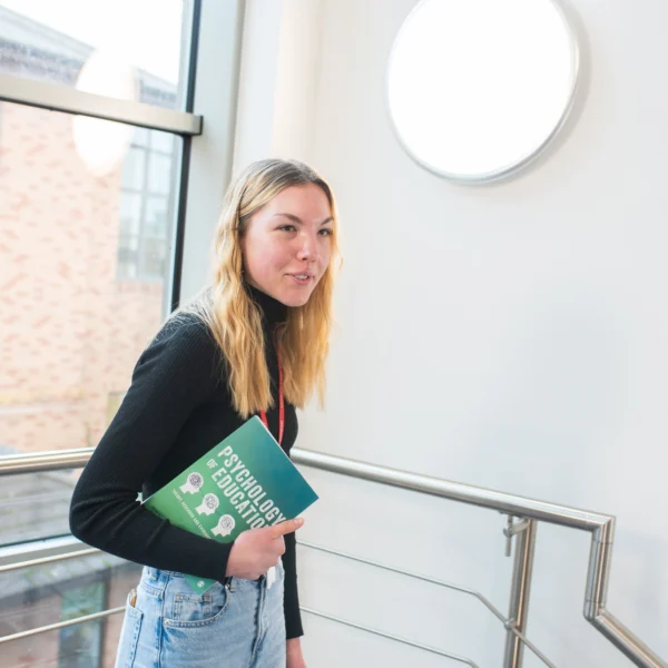 A young woman smiling and holding books on a staircase.