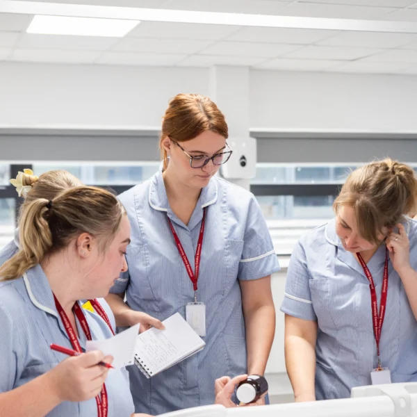 Female nursing students in a classroom setting looking at a watch and notes.