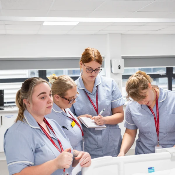 Four nursing students in a hospital setting looking at a patient bed.