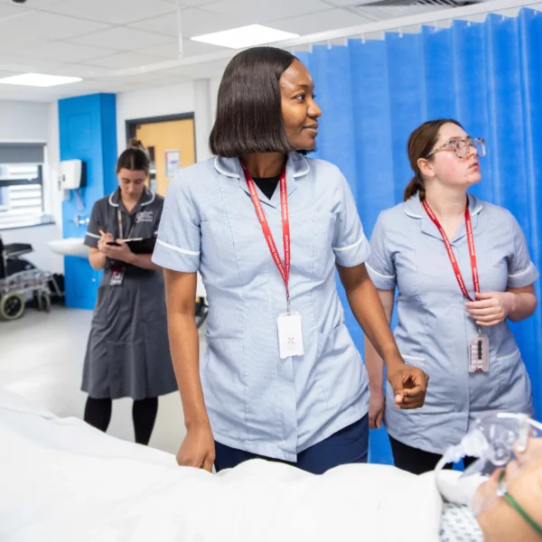 Two healthcare professionals walking down a hospital corridor with a patient in the background.