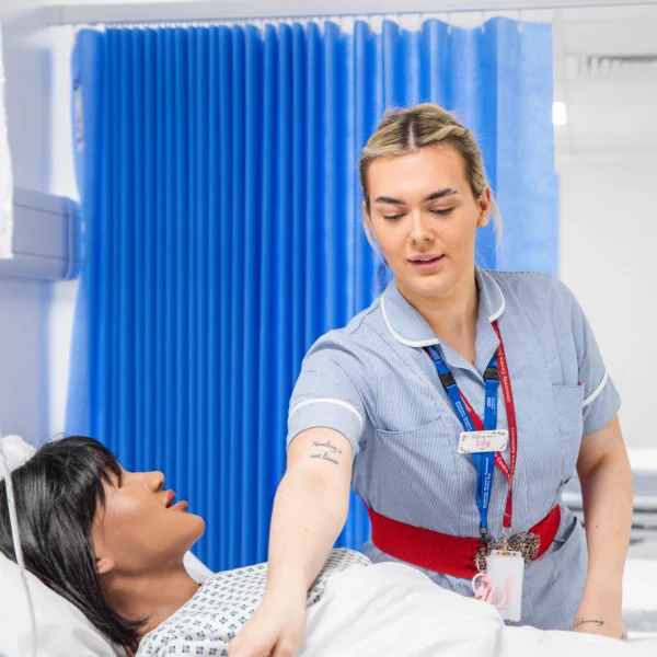 A woman lies in a hospital bed with a female nurse or caregiver standing beside her.