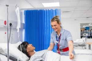 A nurse in a hospital room interacting with a patient lying in bed.