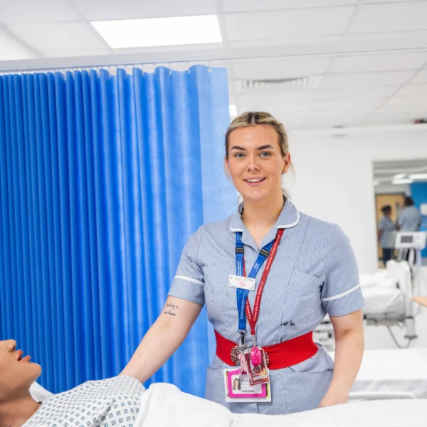 Nurse smiling while standing beside a patient lying in a hospital bed.