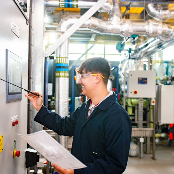A man in a lab coat writing on a machine, another man observing in the background.