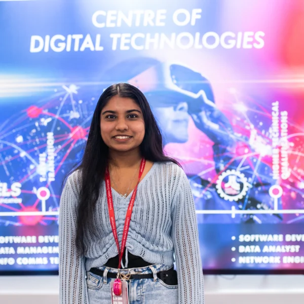 A smiling woman standing in front of a digital screen.
