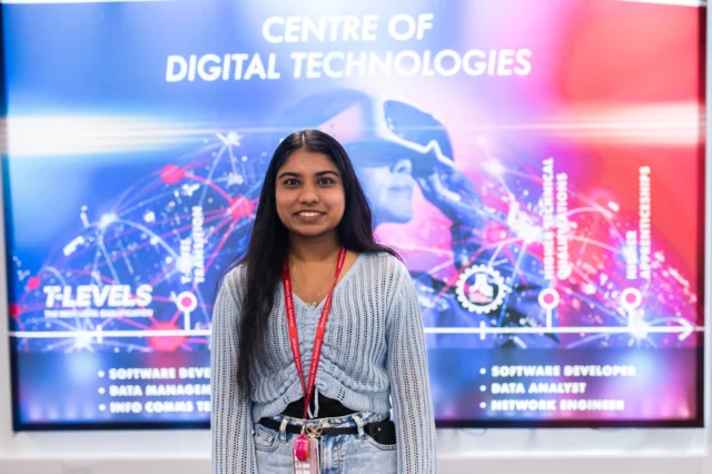 A smiling woman standing in front of a digital screen.