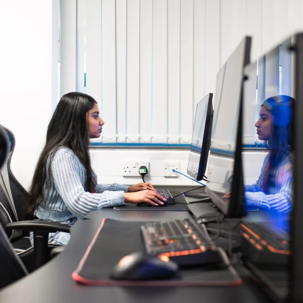 A woman sitting at a computer workstation with multiple monitors.