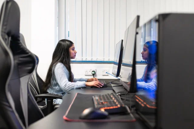 A woman sitting at a computer workstation with multiple monitors.