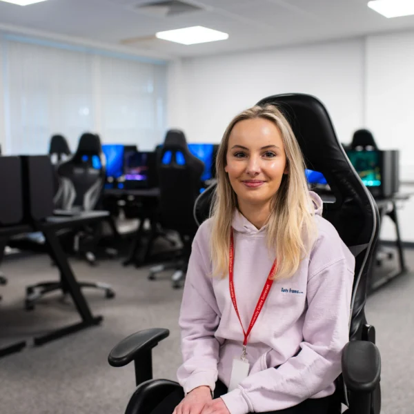 A young woman sitting in a gaming chair in an office with computers.