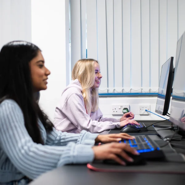Three young women sitting at computers in a classroom setting.
