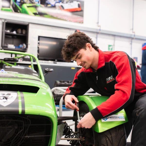 Mechanic working on a green race car in a garage.