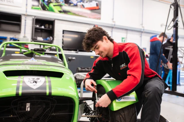 Mechanic working on a green race car in a garage.