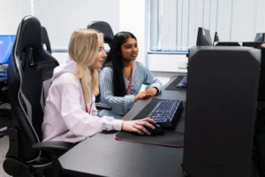 Two young women sitting at a desk with a computer.