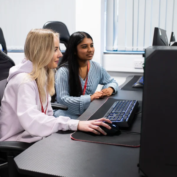Two young women sitting at a desk with a computer.