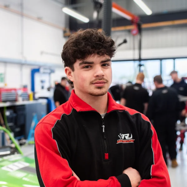 Young man in racing team shirt standing in a garage.