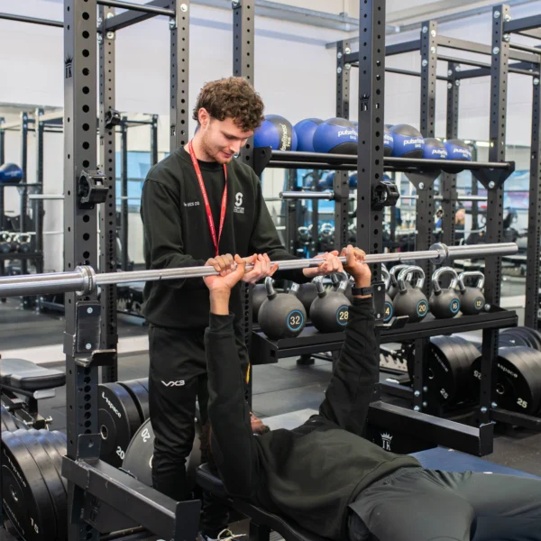Man lifting weights on a bench press with a spotter.