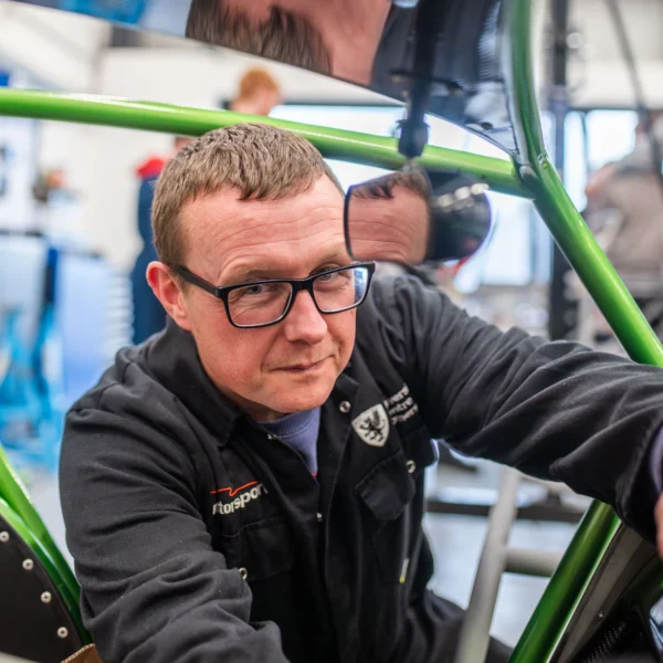 Man in workshop with green metal frame smiling at camera.