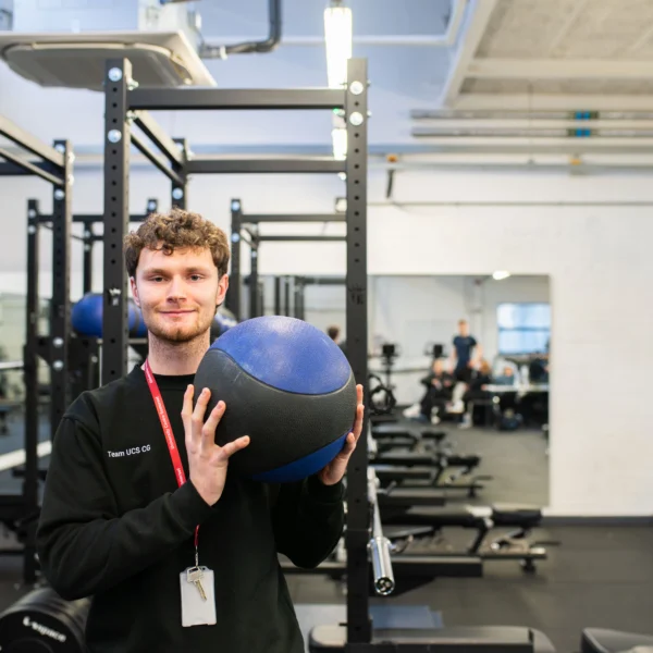 Young man holding a blue and black medicine ball in a gym.
