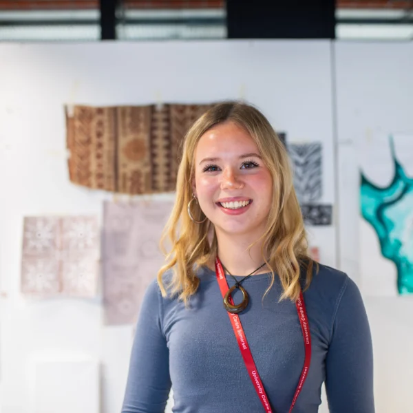 A young woman with blonde hair standing in front of artwork on a wall.