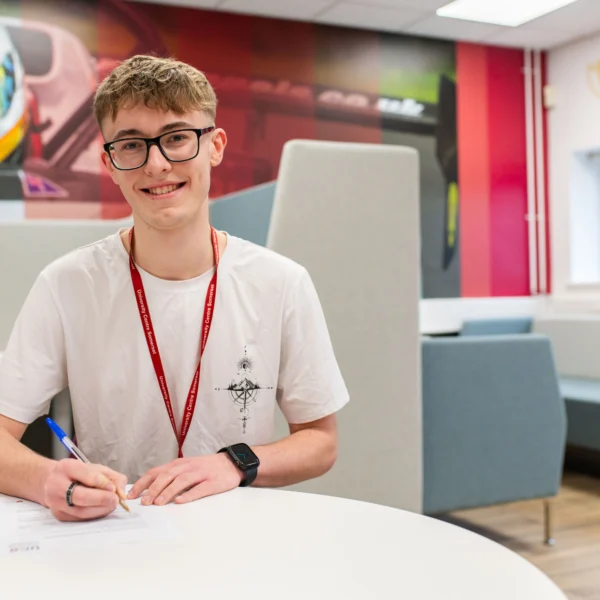 A young man sitting at a table, signing a document with a pen