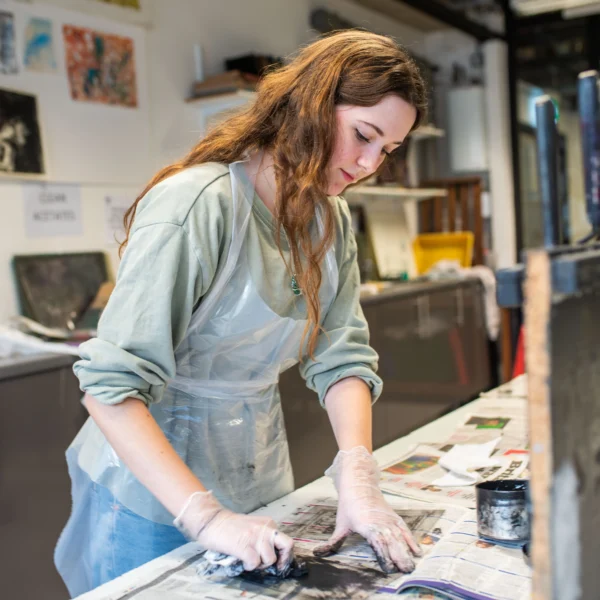 A woman with long hair working on a project, covered in a protective apron.