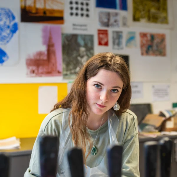 A young woman sitting at a desk in an office or classroom setting.