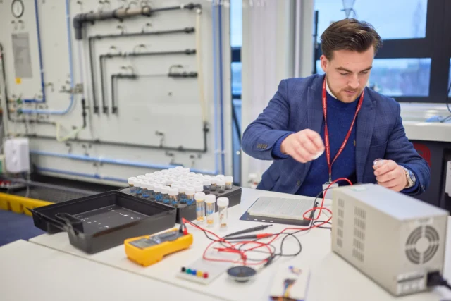 man in a blue suit working on electronics with various tools and equipment.