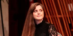 A woman with long brown hair wearing a black top with lace sleeves.