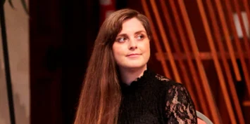 A woman with long brown hair wearing a black top with lace sleeves.