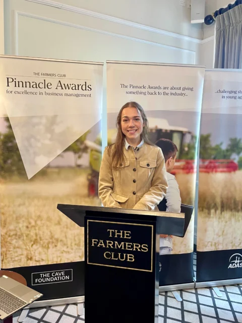 A woman standing behind a lectern with a sign that reads The Farmers Club at the Pinnacle Awards final