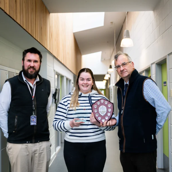 Three people standing in a hallway, a woman holding a plaque.