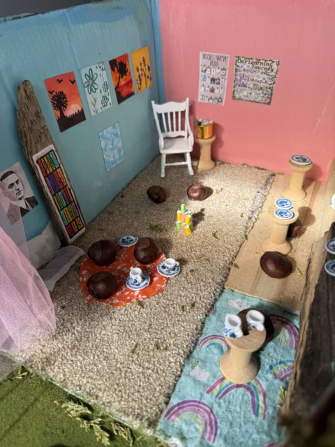 A miniature room with pink and blue walls, decorated with art and pottery.