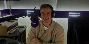 A man wearing headphones sitting next to a microphone in a radio studio.