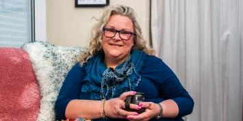Woman with glasses sitting on a couch holding a phone.