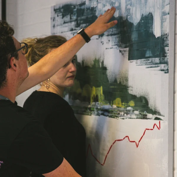 Two people hanging a large abstract painting on a wall.