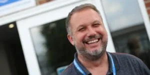 A smiling man with a short cut beard and moustache, wearing a blue lanyard.