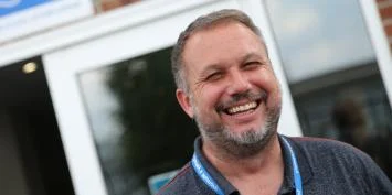 A smiling man with a short cut beard and moustache, wearing a blue lanyard.