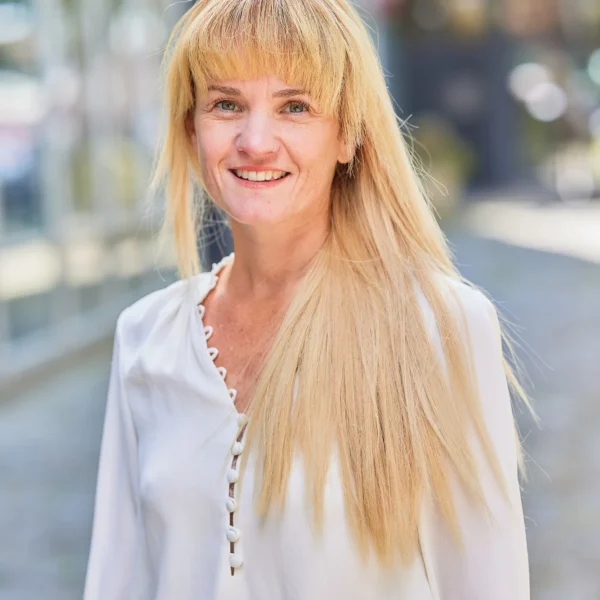A woman with long blonde hair and bangs smiles at the camera.