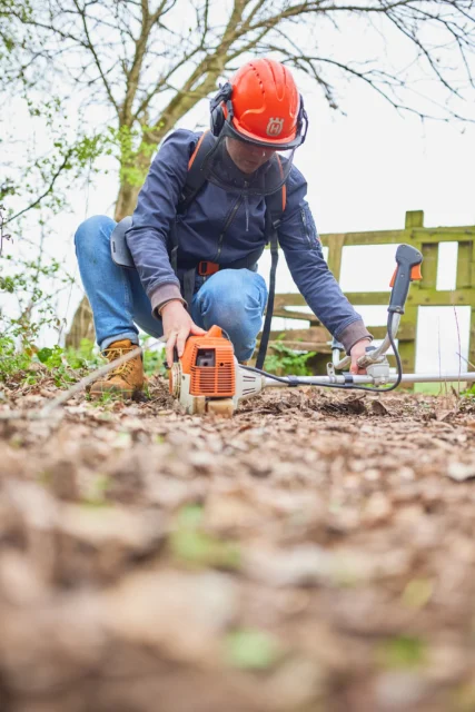 Man in orange helmet and blue jacket using chainsaw on ground