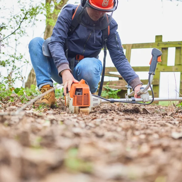 Man in orange helmet and blue jacket using chainsaw on ground