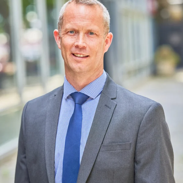 A professional man in a grey suit standing outside a modern building.