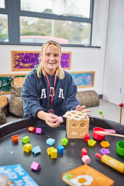 A young girl playing with wooden blocks and toys on a table.
